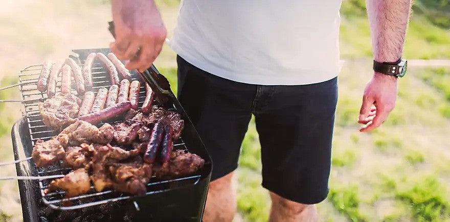 Man turning cuts of meat and franks on a charcoal grill.