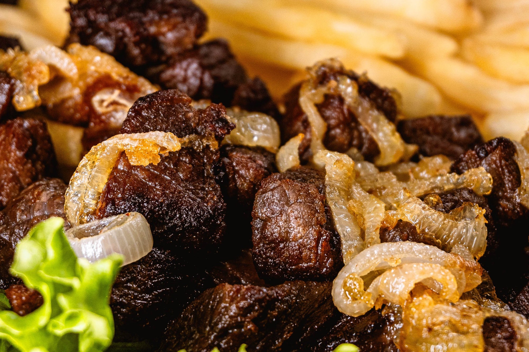 A close up image of carne asada with onions and a side of fries