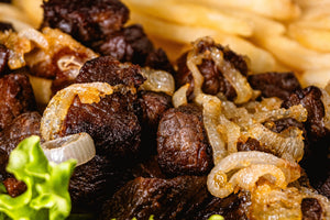 A close up image of carne asada with onions and a side of fries