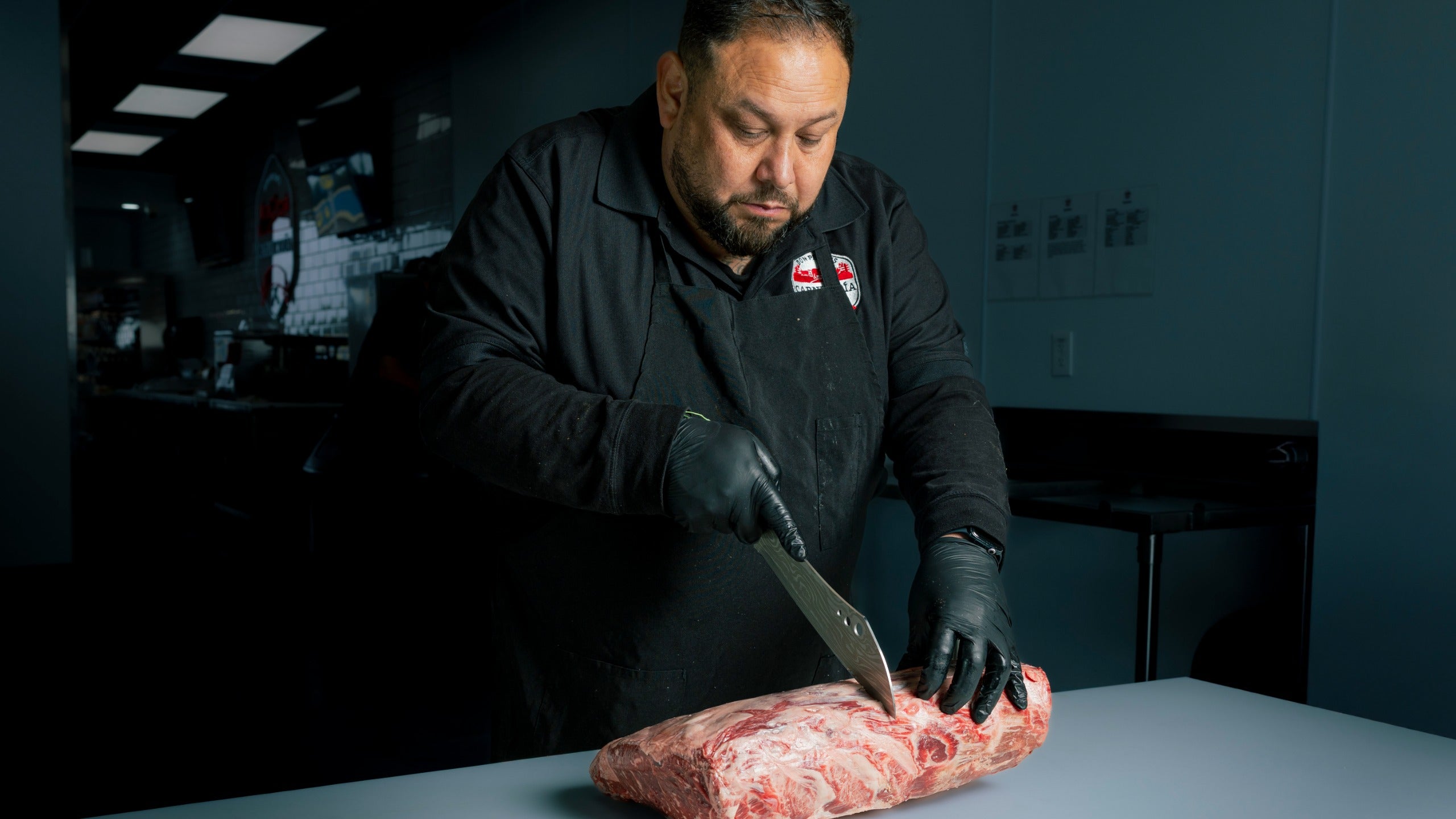 Butcher cutting raw meat with a large knife in a kitchen setting