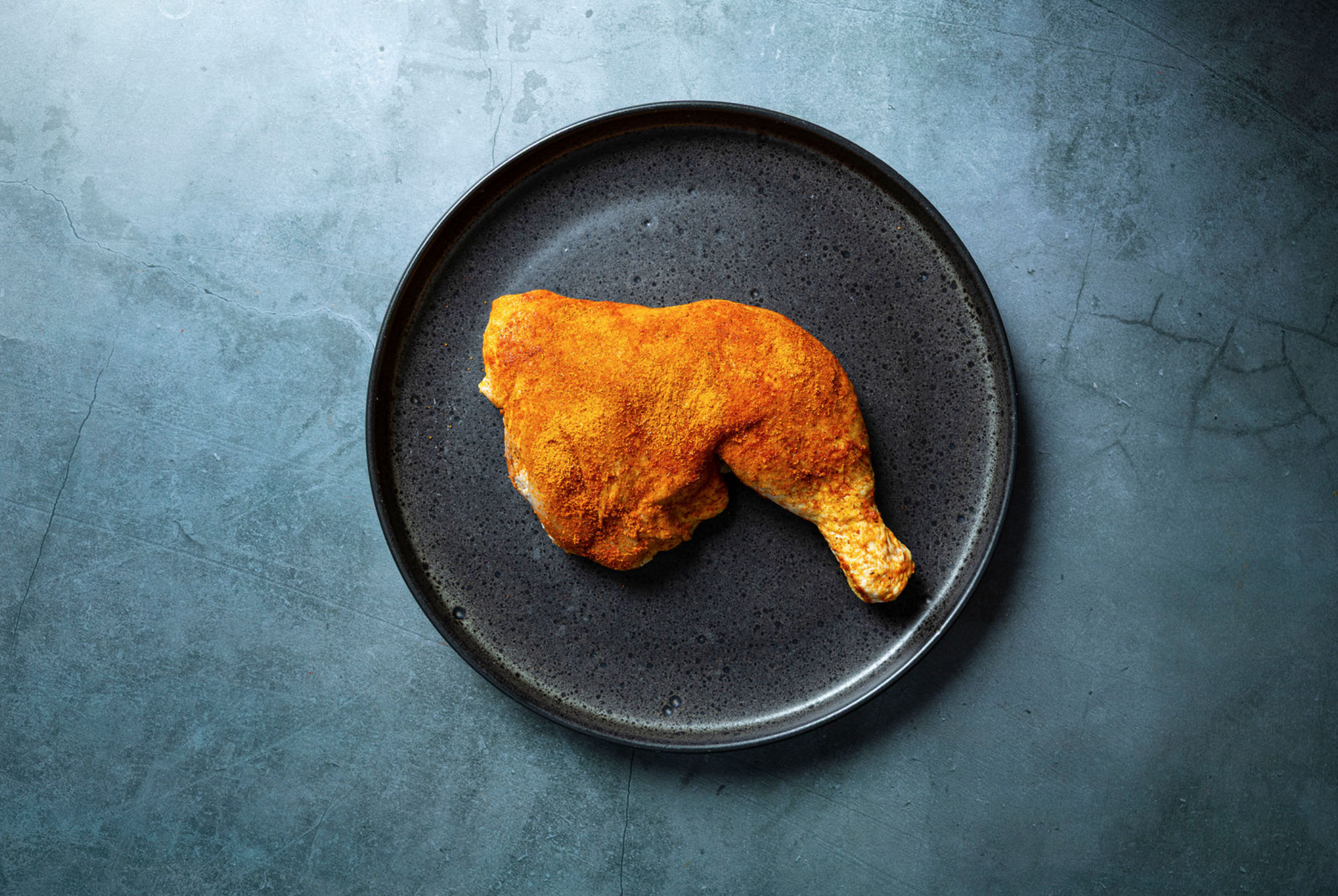 Marinated chicken leg on a dark plate with a textured gray background