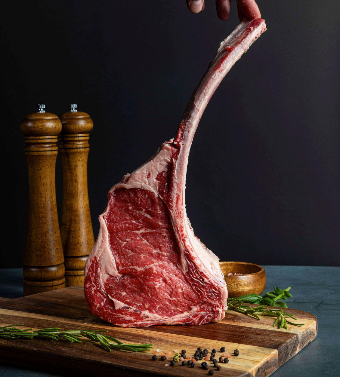 a T-bone steak on ice next to a nice, herbs, and peppers