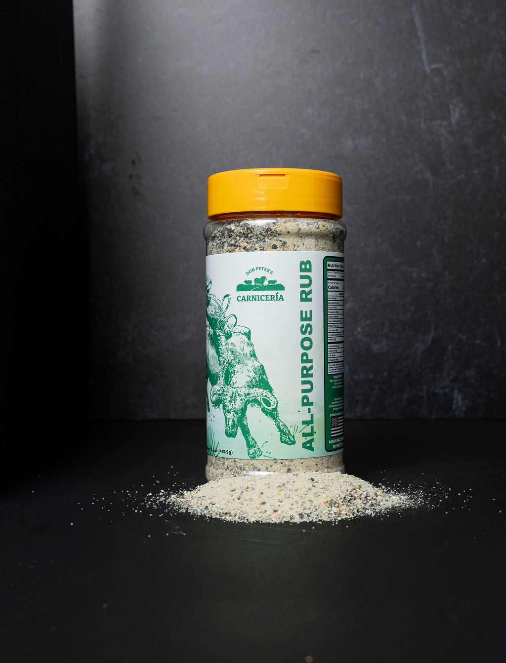 A shaker of All Purpose RC Rub with a pile of the seasoning beside the shaker.