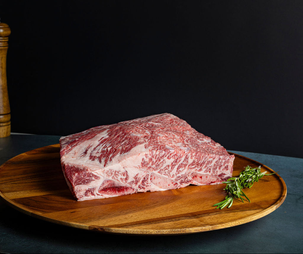 A thick set of raw Prime beef dino ribs and herbs on a round wooden tray