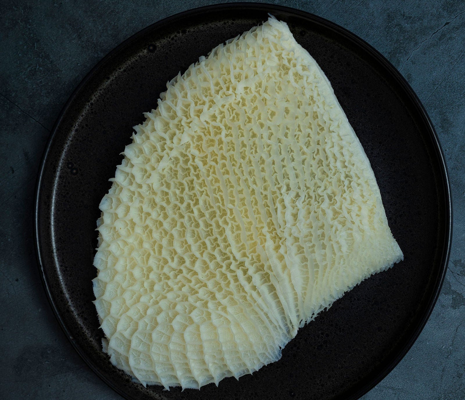 A white cut of beef honeycomb tripe on a black plate