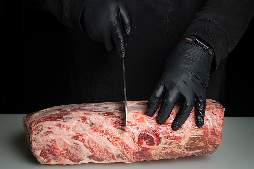a butcher cutting into a piece of lamb meat