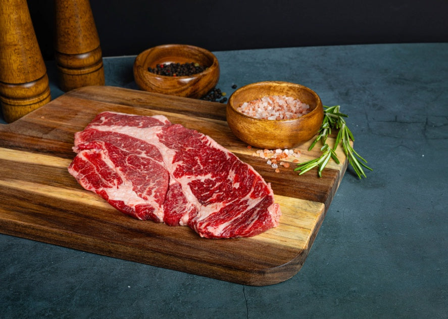 chuck eye steak on a cutting board next to salt and rosemary
