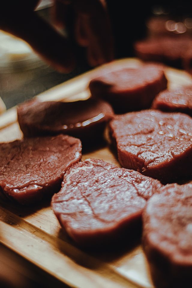 A number of beef cuts being seasoned on a cutting board.