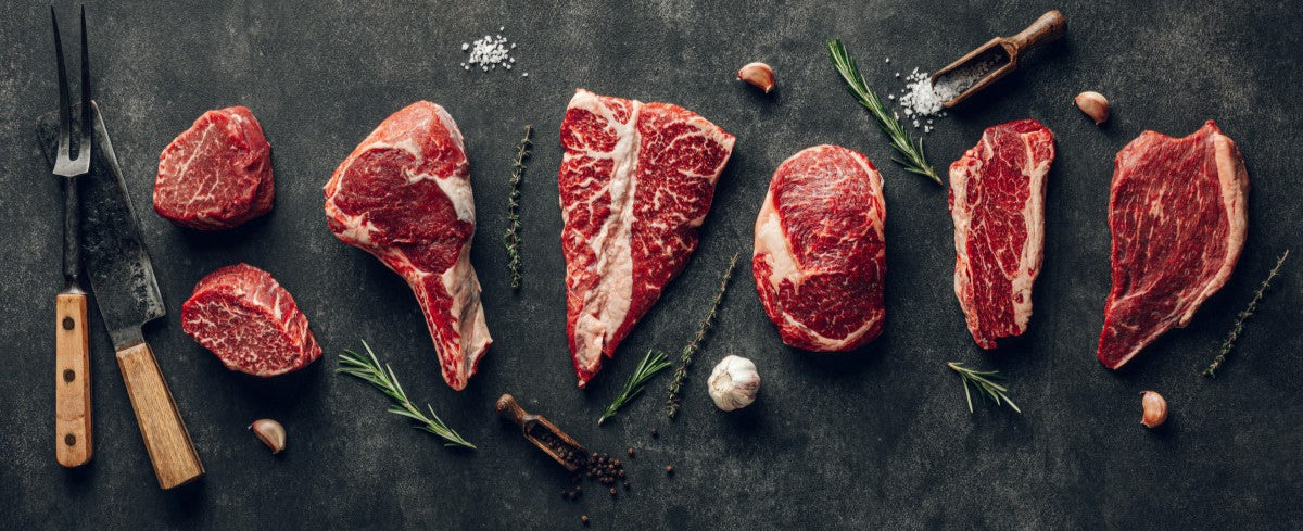 different cuts of raw meat lined up with herbs and knives
