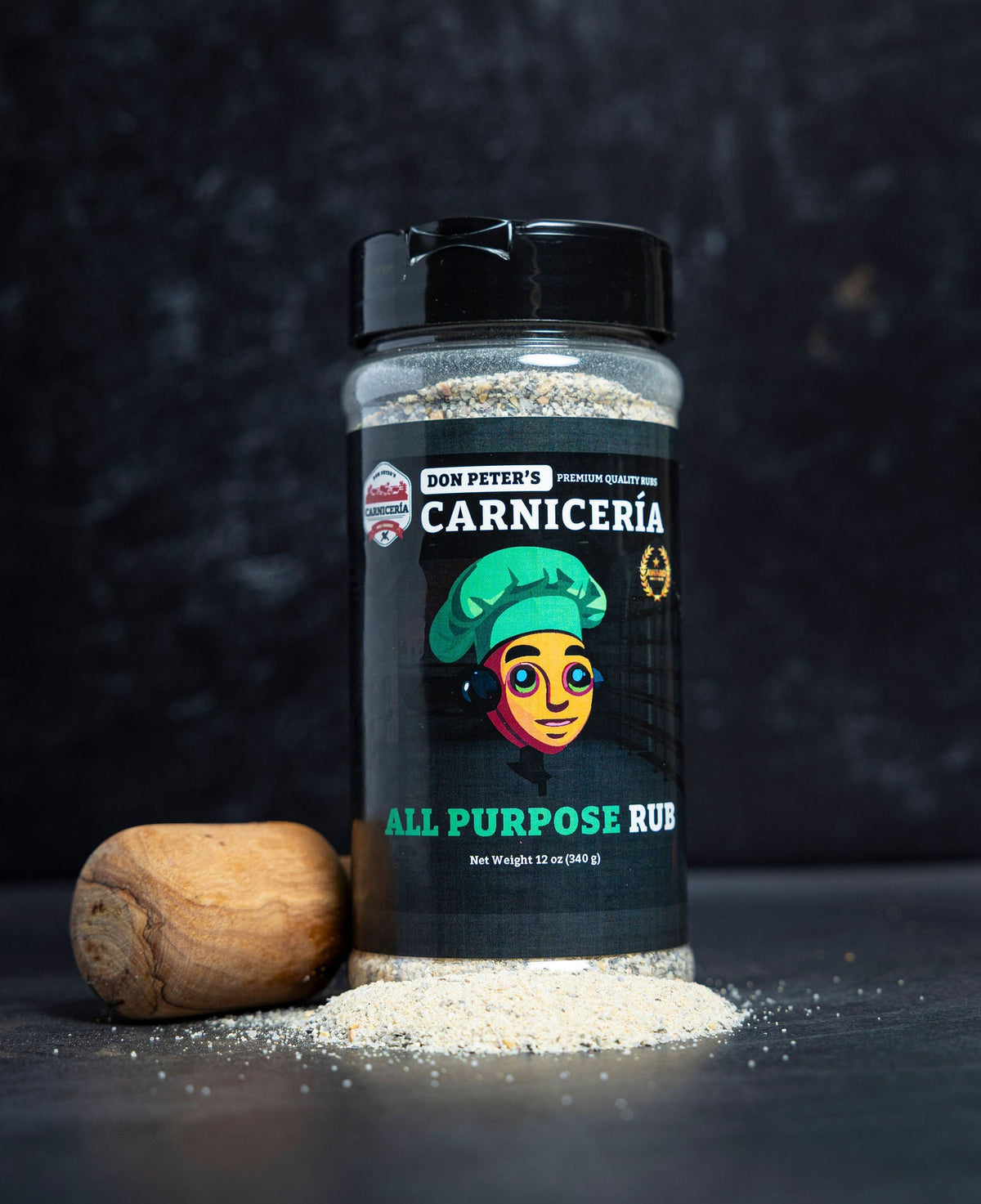 A shaker of Don Peter’s All Purpose Rub with a pile of the spice beside it and a pestle behind it.