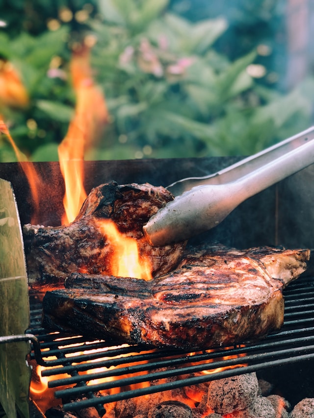 tongs grilling steaks over a flame